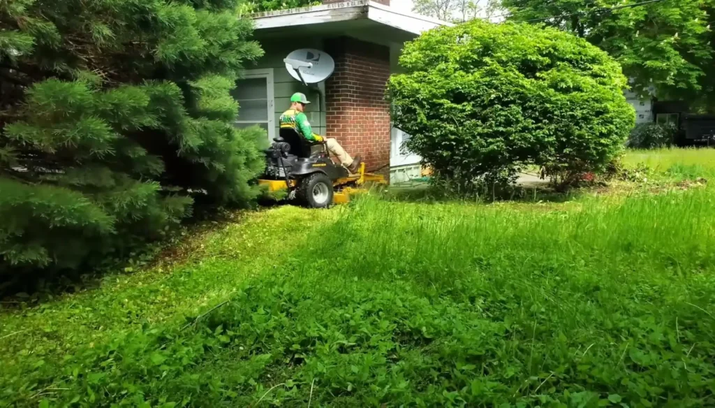 Waco lawn services trimming thick grass around bushes and trees with a ride-on mower