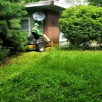 Waco lawn services trimming thick grass around bushes and trees with a ride-on mower
